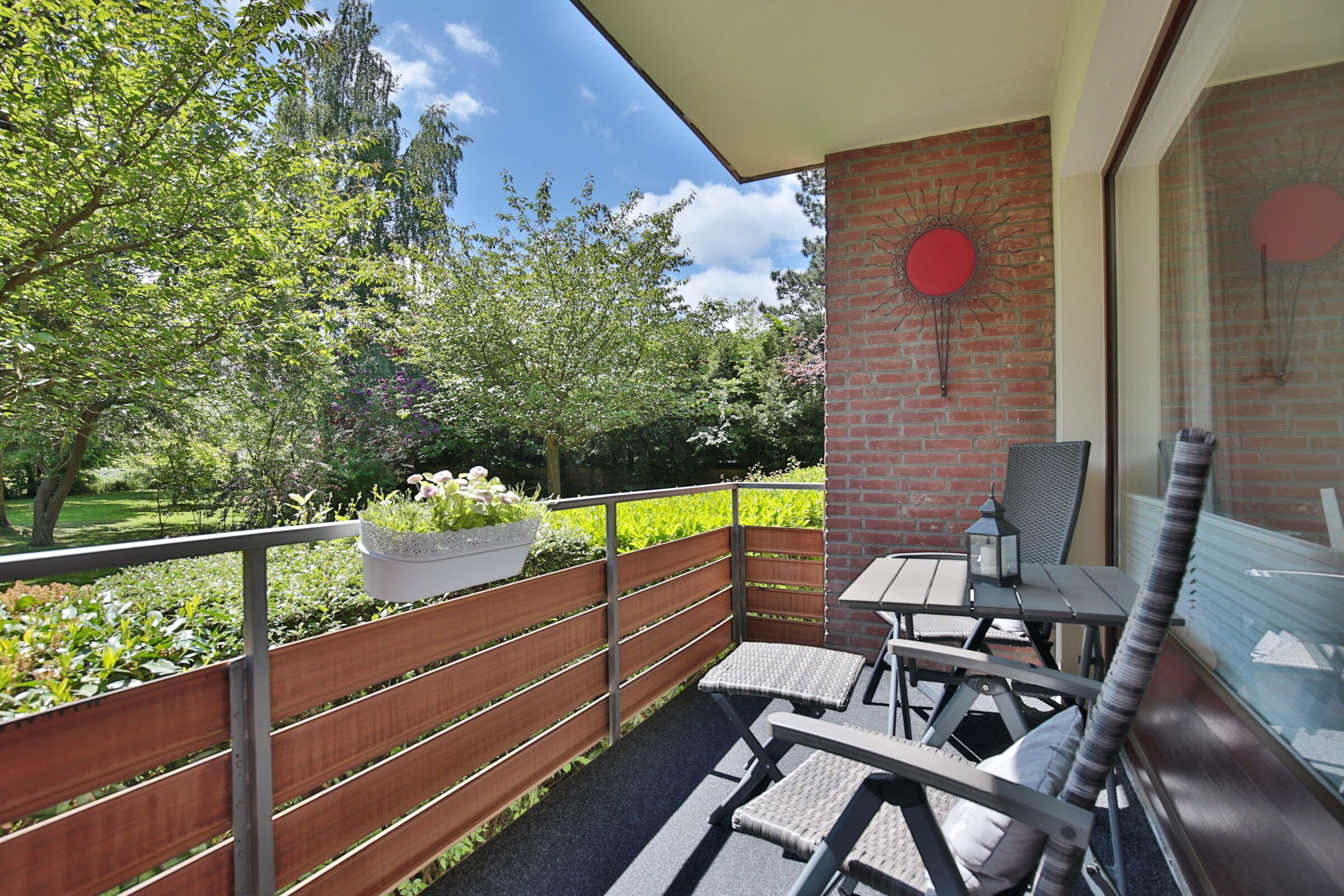 Een balkon met een tafel en stoelen, een bakstenen muur en uitzicht op een tuin.
