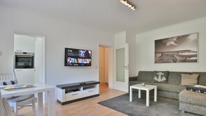 Una sala de estar moderna con una televisión de pantalla plana, un comedor y un sofá gris.