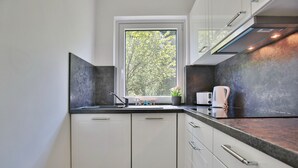 Una cocina moderna con armarios blancos, encimera negra y ventana con vistas a árboles.