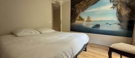 A bedroom with a large bed, a bench, and a painting of a coastal scene.