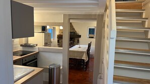 Une cuisine équipée d’un four à micro-ondes, d’une cuisinière et d’un évier, un coin repas avec une table et des chaises, et un escalier.