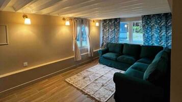 Une pièce avec un plafond en pente, un canapé vert, un tapis à motifs et une fenêtre avec des rideaux.