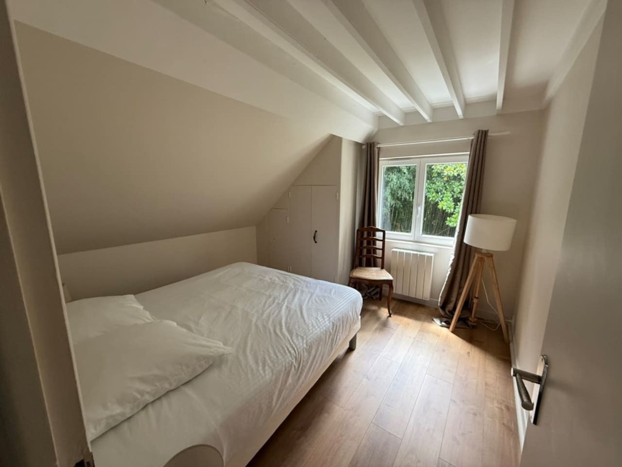 A bedroom with a single bed, a chair, a lamp, and a window with curtains.