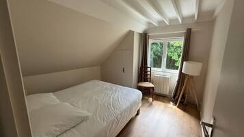 A bedroom with a single bed, a chair, a lamp, and a window with curtains.