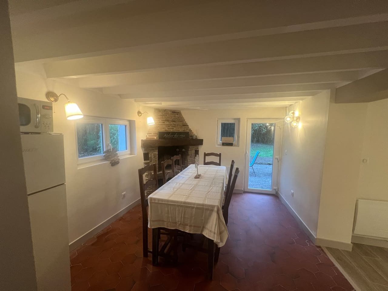 Un coin repas avec une table dressée pour quatre personnes, une cheminée en pierre et une vue sur l’extérieur grâce à une porte vitrée.