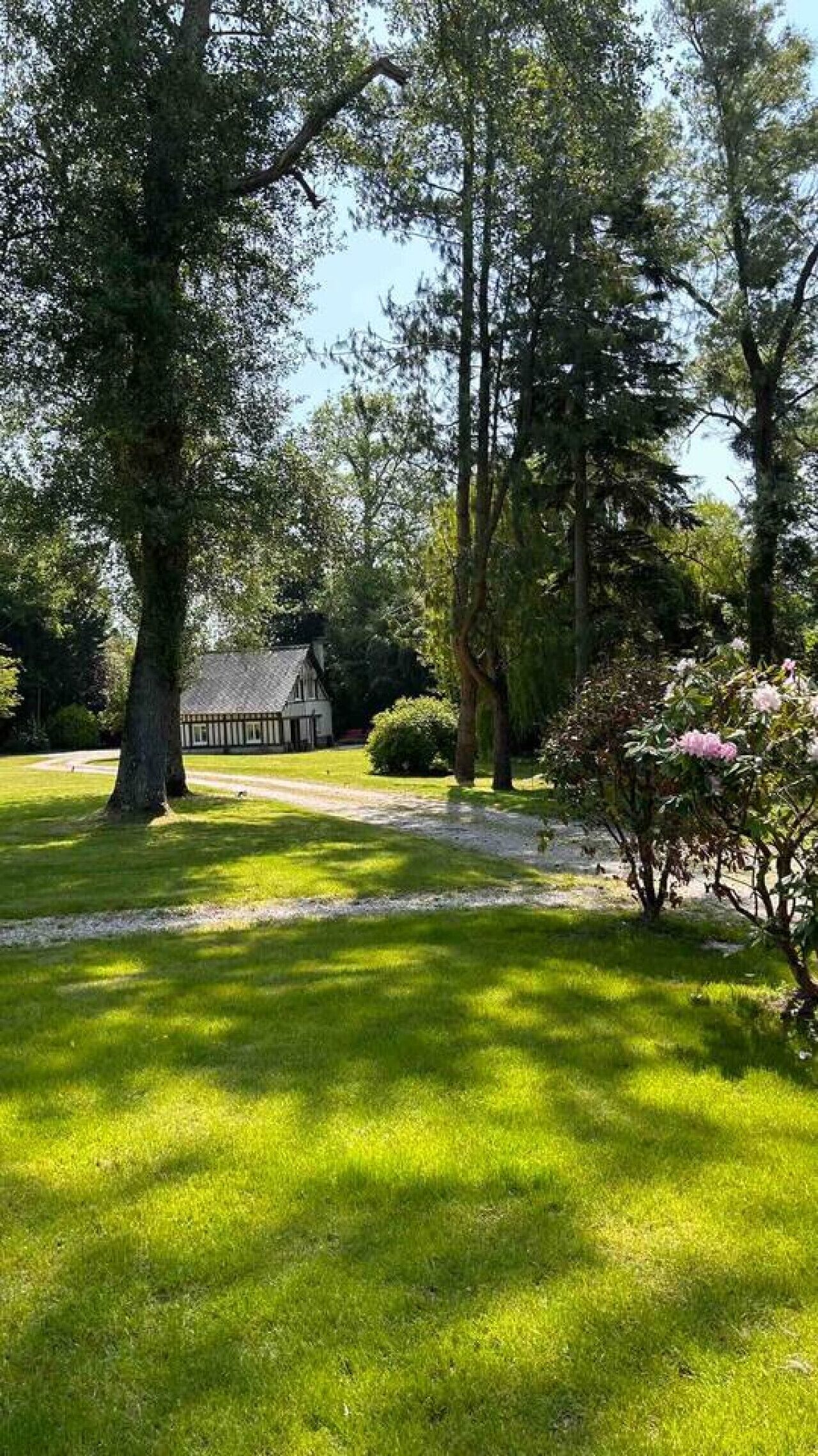 Une maison traditionnelle avec un toit de chaume, entourée d’une pelouse bien entretenue et de grands arbres.
