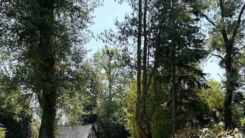 Une maison traditionnelle avec un toit de chaume, entourée d’une pelouse bien entretenue et de grands arbres.