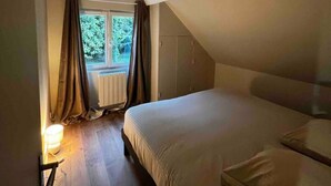 Une chambre avec un plafond en pente, une fenêtre avec des rideaux, un lit et une table de chevet avec une lampe.