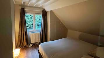 Une chambre avec un plafond en pente, une fenêtre avec des rideaux, un lit et une table de chevet avec une lampe.
