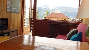 A wooden interior with a TV, a table, and a view of mountains through a window. - Central Apartment for 5, Near Slopes & Shops, Crest-Voland (Crest-Voland)