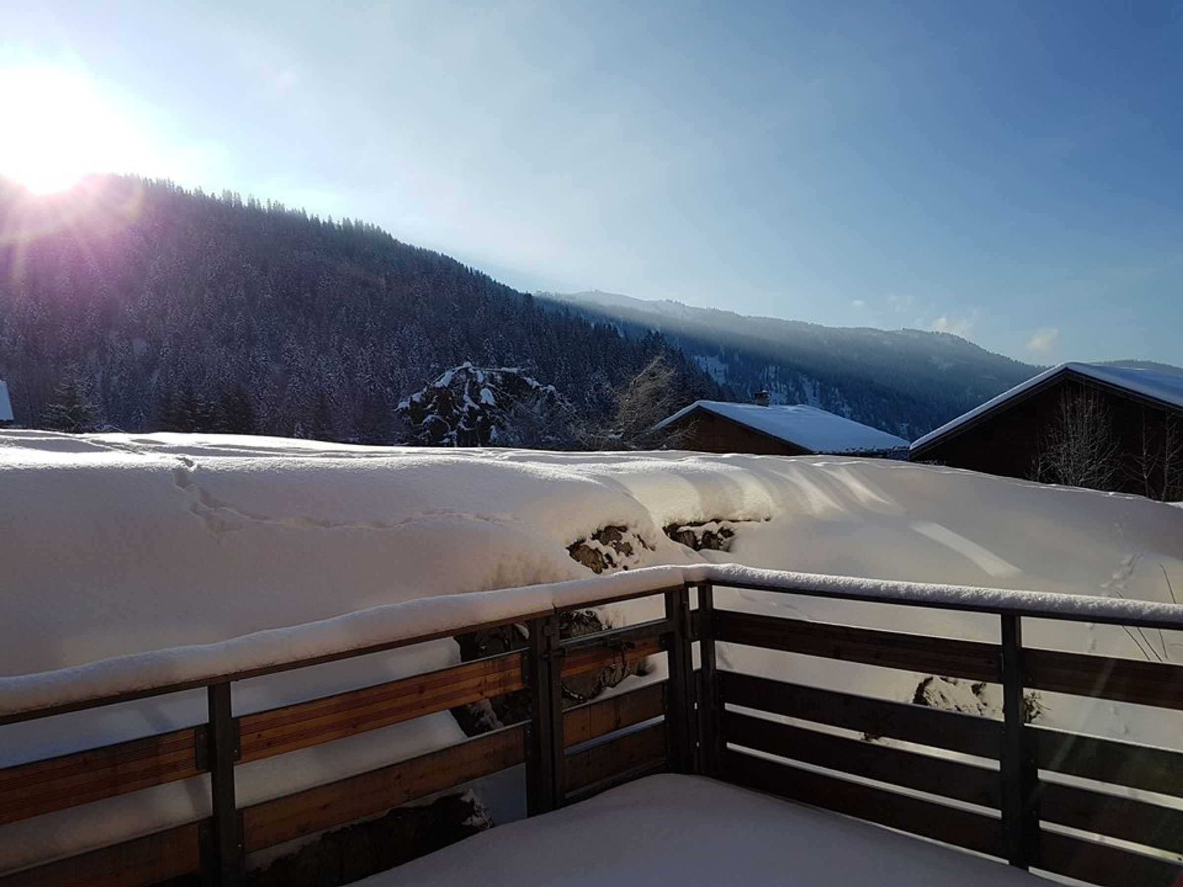 A snow-covered balcony with a wooden railing overlooking a mountainous landscape.