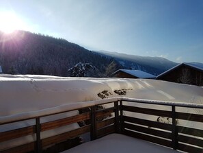 Un balcón cubierto de nieve con baranda de madera que da a un paisaje montañoso.