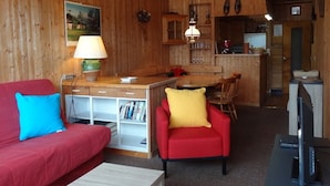 A cozy living area with a red sofa, a red armchair, and a small table. There is a kitchen area with wooden cabinets and a dining table. - Central Apartment for 5, Near Slopes & Shops, Crest-Voland (Crest-Voland)