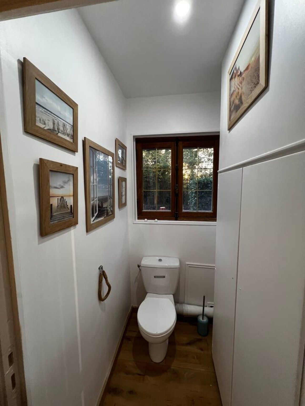 A small bathroom with a toilet, a window, and framed pictures on the wall.