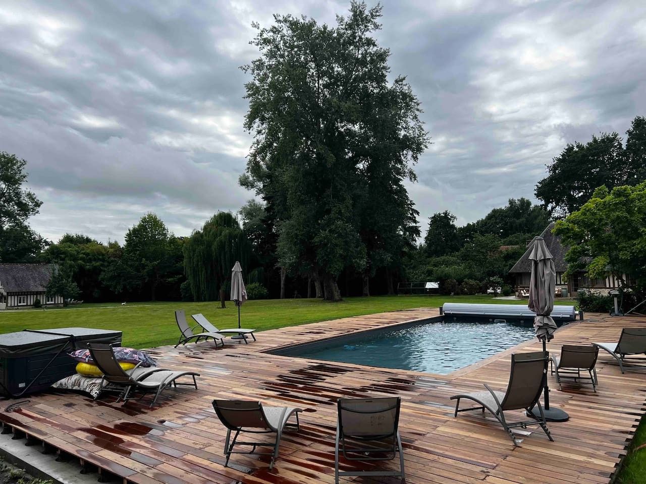 A wooden deck with a swimming pool, lounge chairs, and a covered umbrella.