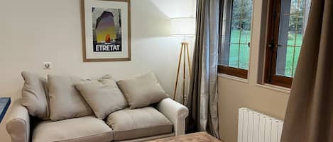 Een woonkamer met een bank, een houten salontafel, een vloerlamp en een raam met gordijnen.