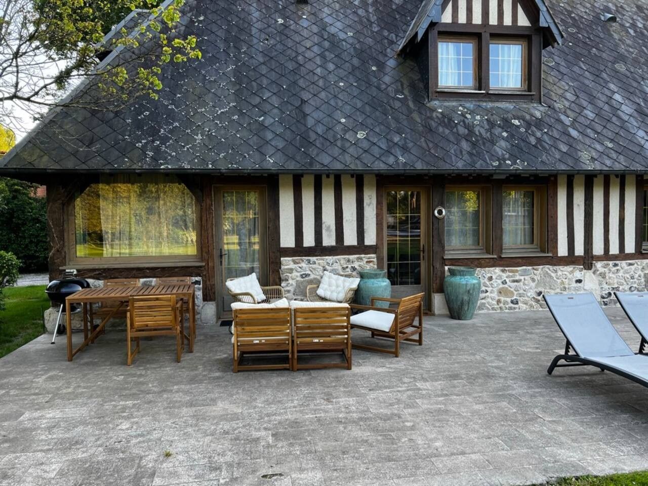 A house with a stone facade, a dark tiled roof, and a patio with outdoor furniture.
