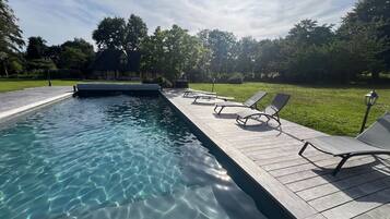 A swimming pool with clear water, surrounded by a wooden deck with lounge chairs.