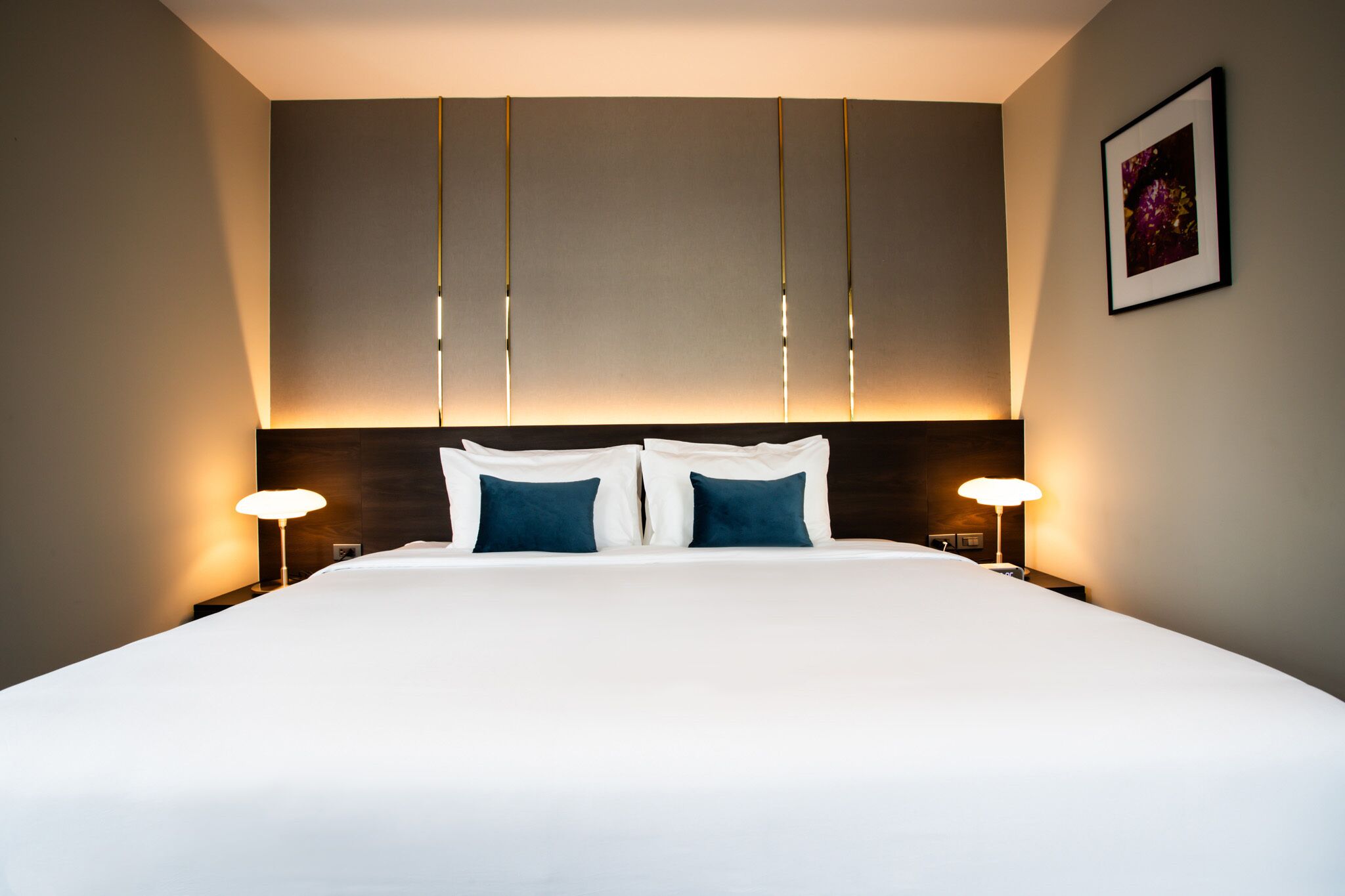 Una cama grande con sábanas blancas y dos almohadas azules, con dos lámparas de noche a cada lado.