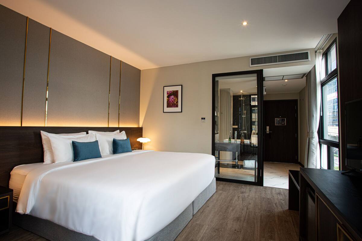 Quarto de hotel moderno com uma cama grande, uma escrivaninha e um banheiro visível por uma porta aberta.