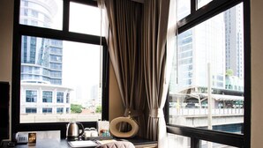 A modern hotel room with a large window, a desk with a kettle, a chair, and a view of the cityscape. - SAM E Hotel Bangkok Sathorn (Bangkok)