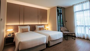 A hotel room with two beds, a nightstand with a lamp, a chair, and a large window with curtains. - SAM E Hotel Bangkok Sathorn (Bangkok)