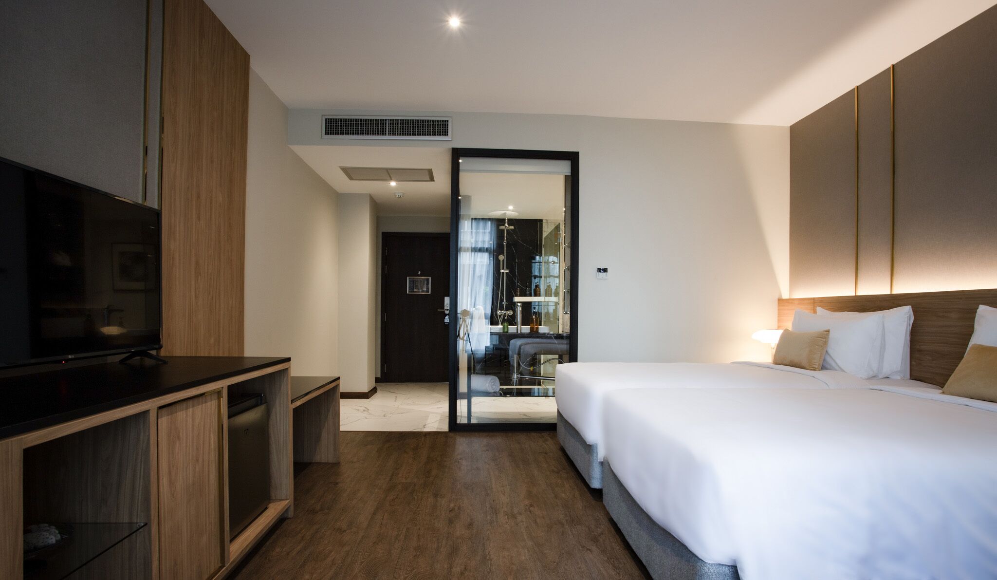 Habitación de hotel con cama, televisor, aparador de madera y baño visible a través de una puerta abierta.