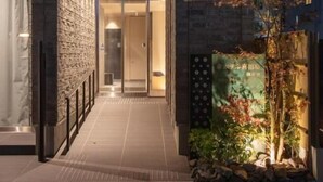 A building entrance with a stone facade, a glass door, and a small garden area with plants. - kyohotel kishotei goshominami (Kyoto)
