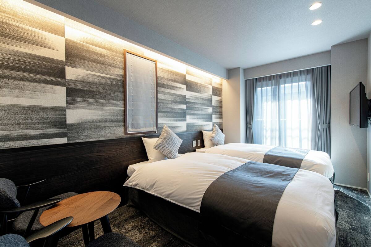 Una habitación de hotel moderna con dos camas, una mesita de madera y una gran obra de arte abstracta en la pared.