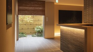 A modern interior with a reception desk, a large flat-screen TV, and a sliding door leading to a garden. - kyohotel kishotei goshominami (Kyoto)