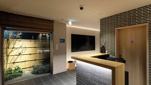 A reception area with a wooden counter, a black wall-mounted screen, a door with a 'No Entry' sign, and a view of a bamboo fence outside. - kyohotel kishotei goshominami (Kyoto)
