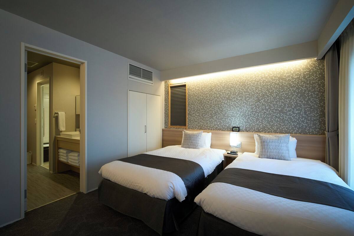 Habitación de hotel con dos camas, baño y pasillo.