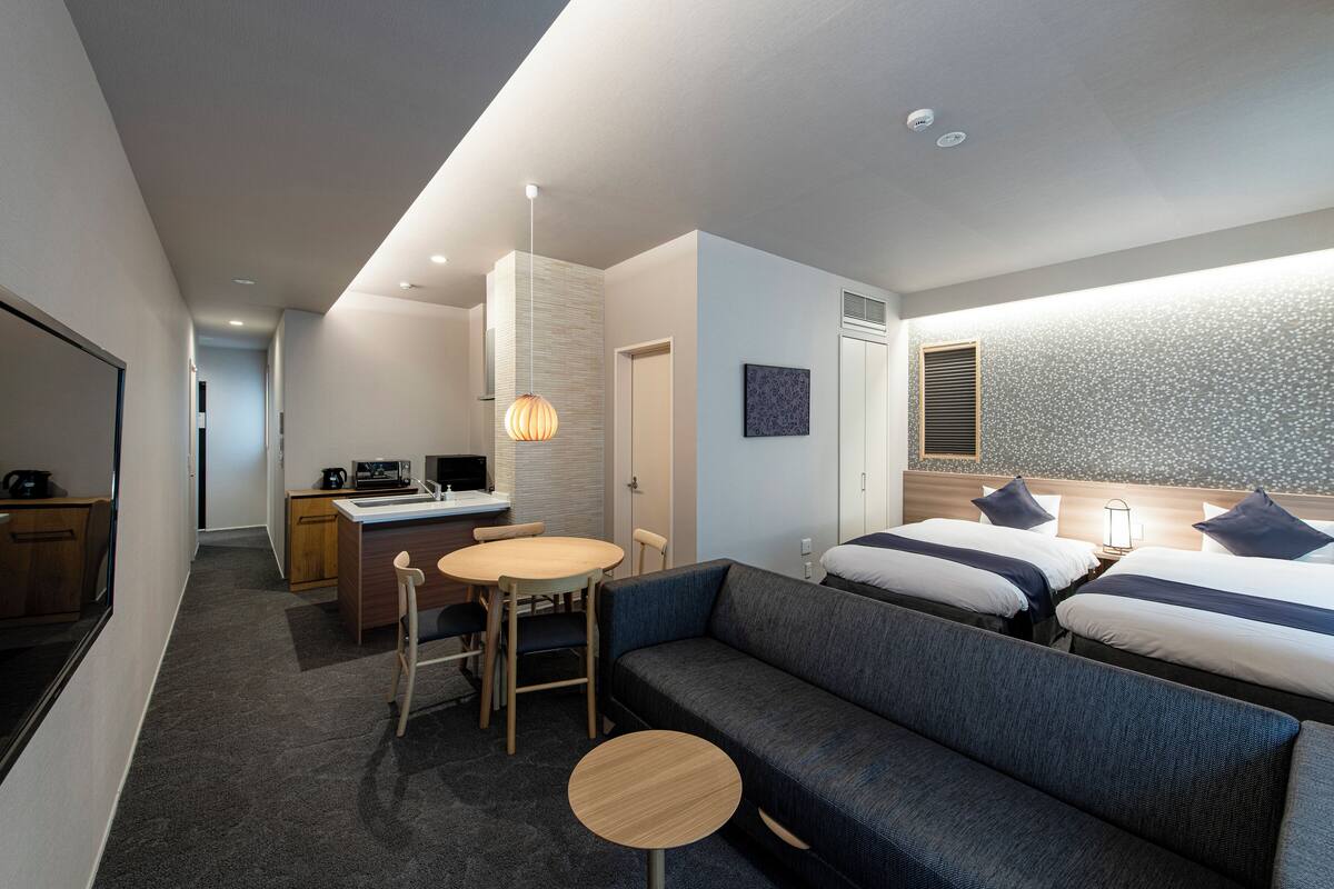 Habitación de hotel moderna con sofá, dos camas, escritorio y un pequeño comedor.