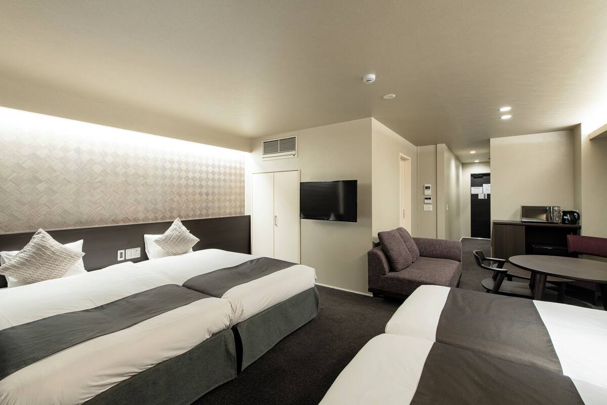 Habitación de hotel con dos camas, un sofá, una mesa de comedor y un televisor.