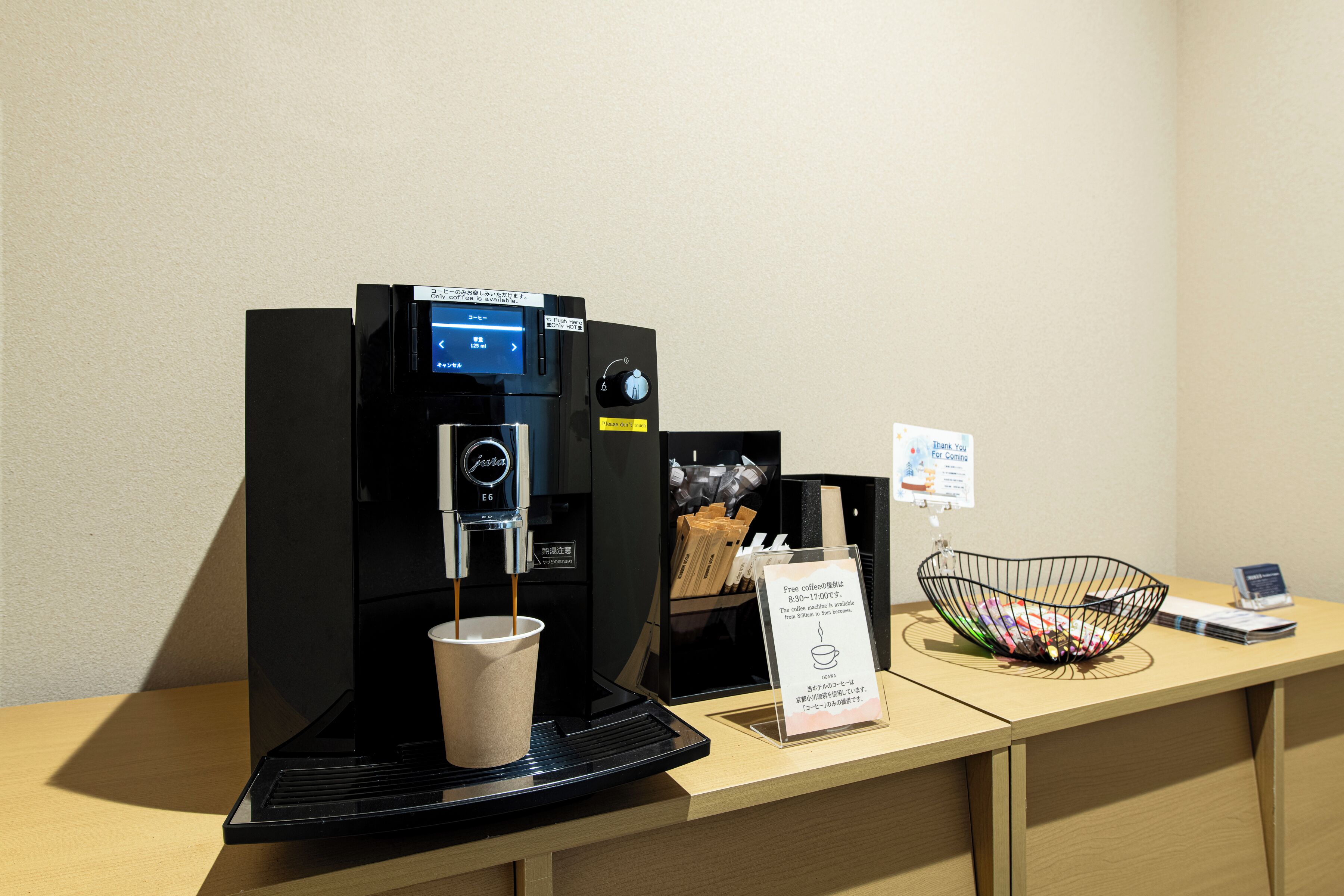 A coffee machine with a cup, a menu board, and a basket of snacks on a wooden counter.
