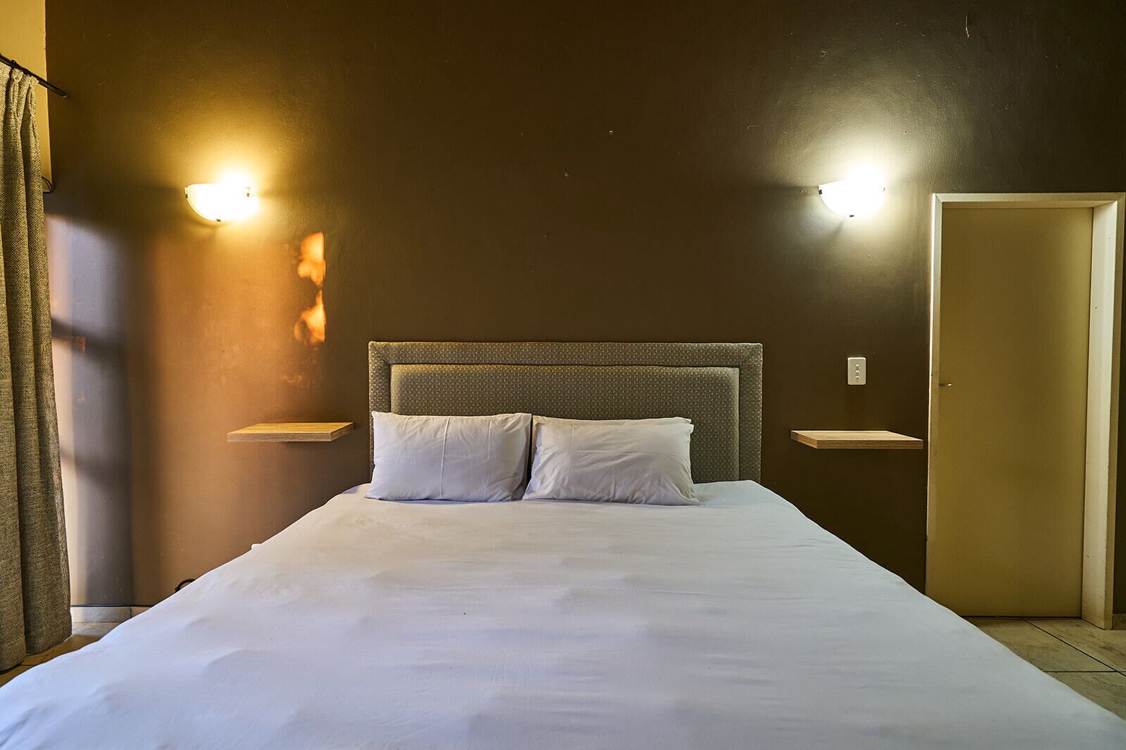 Une chambre d’hôtel avec un grand lit, deux tables de chevet, une tête de lit et deux appliques murales.