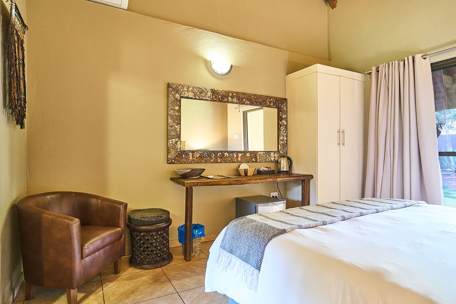 Un dormitorio con cama, un escritorio de madera, una silla, un cubo de basura, un espejo y un armario.