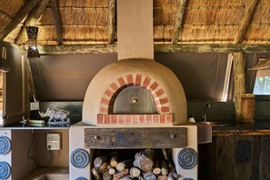A rustic kitchen with a wood-fired oven, a thatched roof, and a rustic wooden counter. - Sable Ranch Bush Lodge  (Brits)