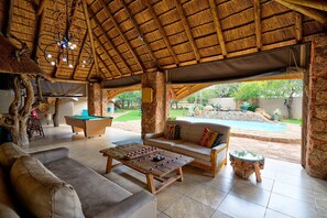 A pool area with a thatched roof, a pool table, a sofa, and a wooden coffee table. - Sable Ranch Bush Lodge  (Brits)