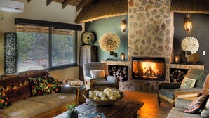 A cozy living room with a stone fireplace, comfortable seating, and a large window overlooking a garden.