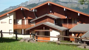 A chalet-style building with a sloped roof, wooden balconies, and a mountain backdrop. - Cozy Studio for 4, Near Cernix Center and Slopes (Crest-Voland)