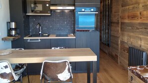 A modern kitchen with dark cabinetry, a built-in oven, and a coffee machine. - Cozy Studio for 4, Near Cernix Center and Slopes (Crest-Voland)