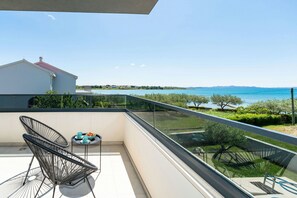 A balcony with a view of a lake and distant mountains, a chair, and a small table with a tray.
