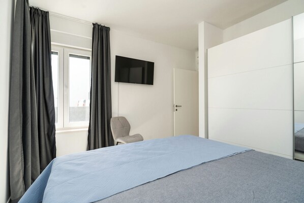 A bedroom with a bed, a chair, a TV, and a wardrobe.