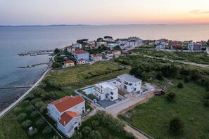 An aerial view of a coastal residential area with houses, a pier, and a clear view of the sea.