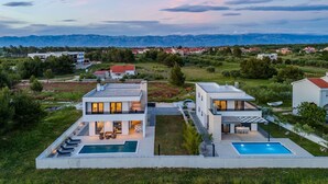 Une maison moderne à deux étages, dotée d’une piscine et d’un espace extérieur aménagé pour se détendre.