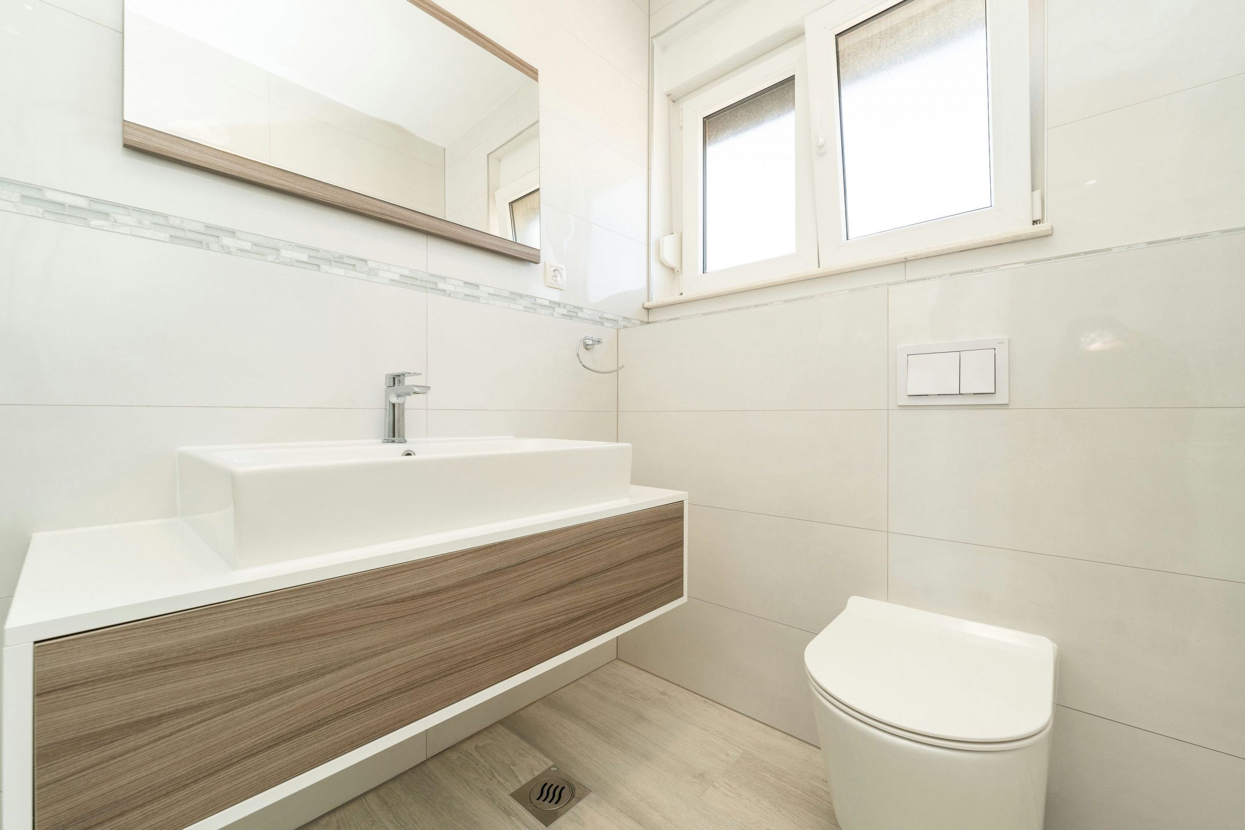 A modern bathroom with a white sink, wooden vanity, and a white toilet.