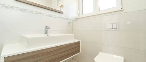 A modern bathroom with a white sink, wooden vanity, and a white toilet.