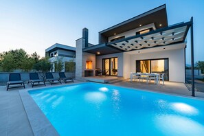 Une maison moderne dotée d’une piscine, d’un espace salon extérieur et d’un patio couvert.