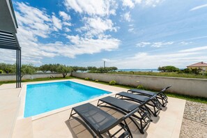 A swimming pool with lounge chairs, a view of the sea, and a clear sky.